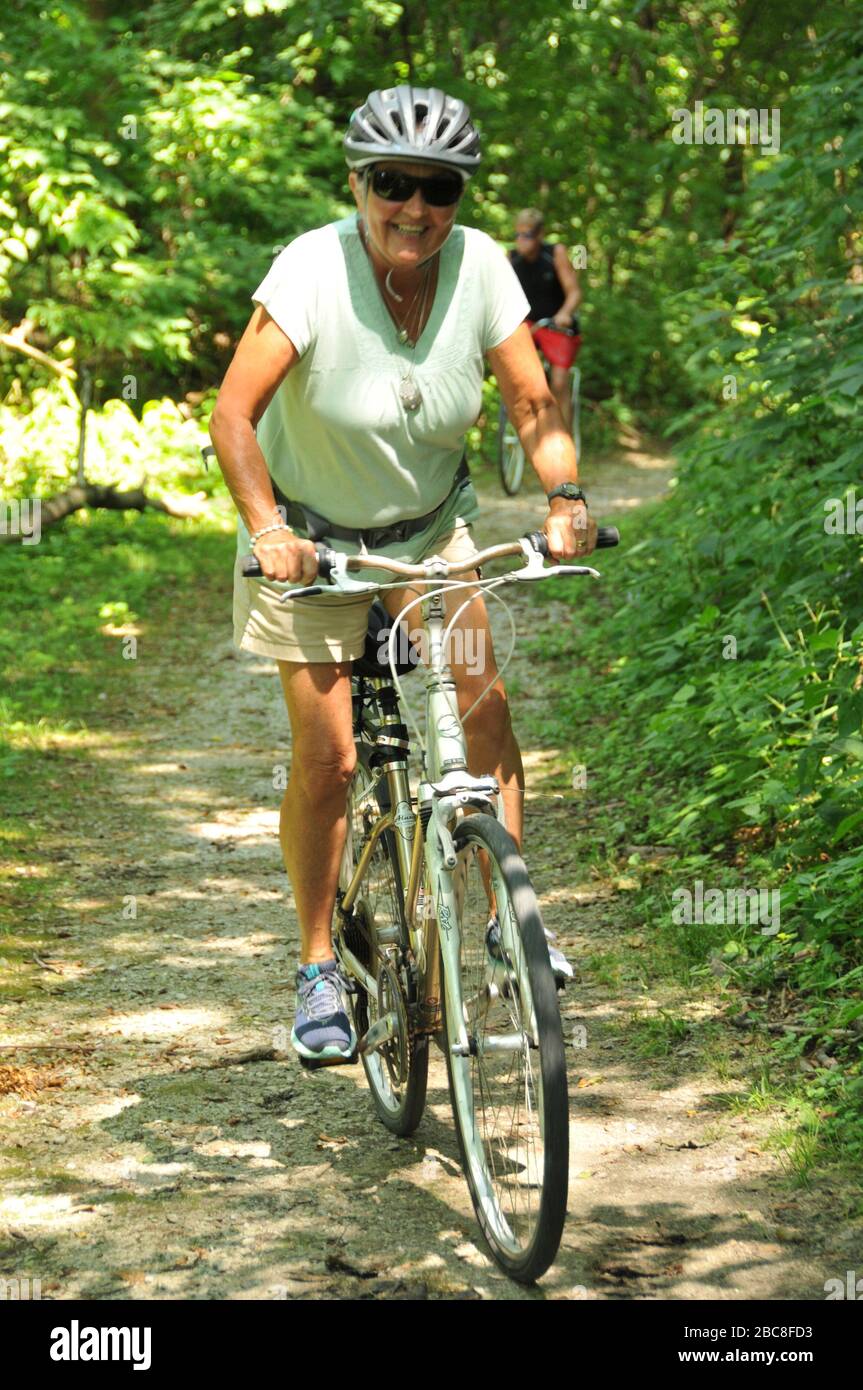 Donna di mezza età che guida una bicicletta su un sentiero attraverso i boschi indossando un casco. Foto Stock