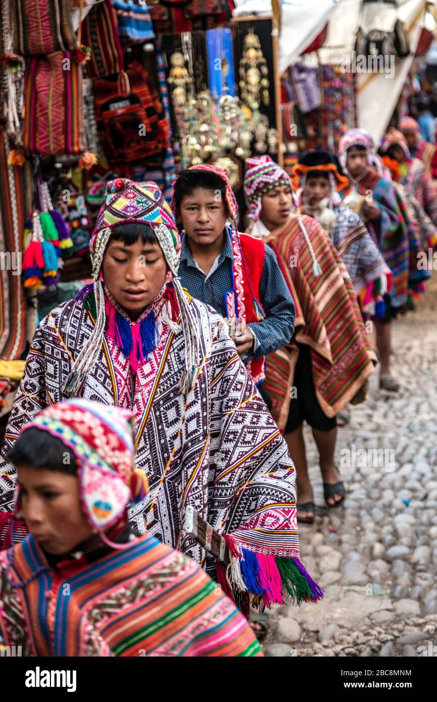 Processione di ragazzi Quechua camminando attraverso bancarelle venditore verso la chiesa, Pisac Domenica mercato, Pisac, Perù Foto Stock
