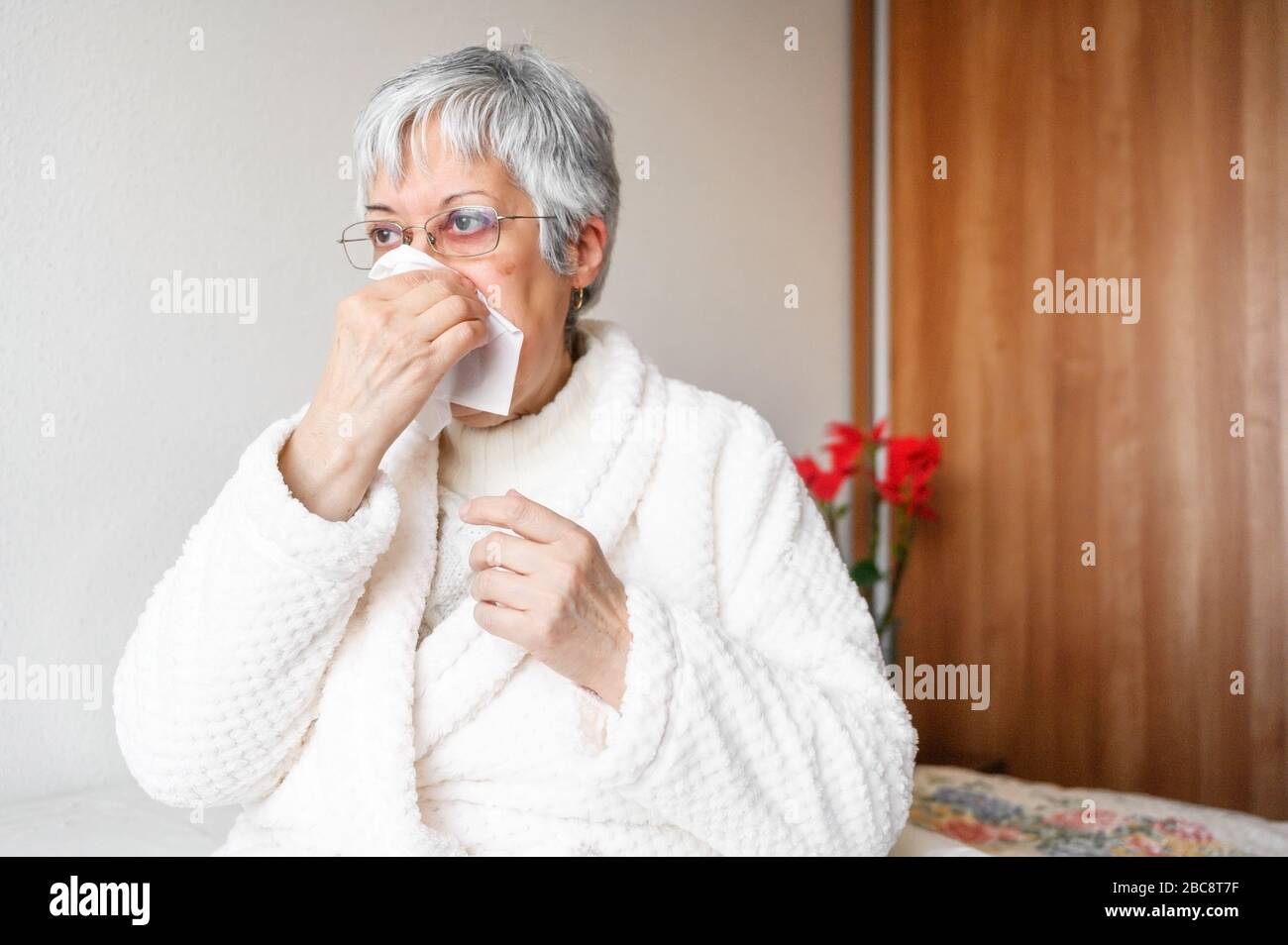 Pandemia di coronavirus. Salute, influenza, igiene e concetto di persone. Donna anziana malata con carta straccio che soffia il naso a casa . Foto Stock