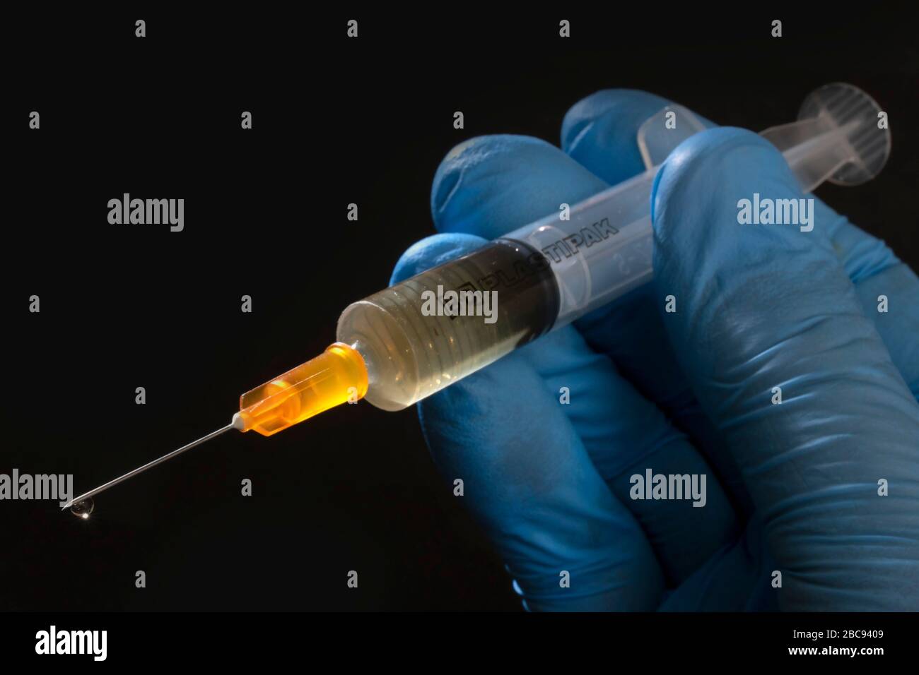 Siringa ipodermica e ago, tenuti da una mano chirurgica blu e utilizzati per somministrare vaccini Foto Stock