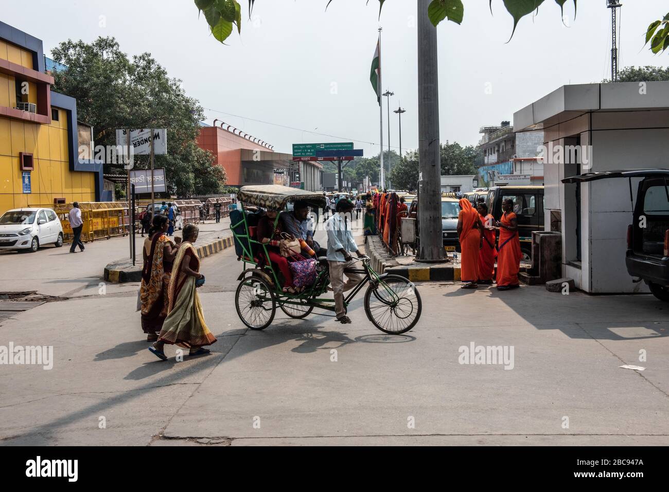 Un gruppo di persone fuori dalla stazione ferroviaria di Nuova Delhi, a piedi da e per il terminal, in una giornata calda, con un risciò in primo piano. Foto Stock