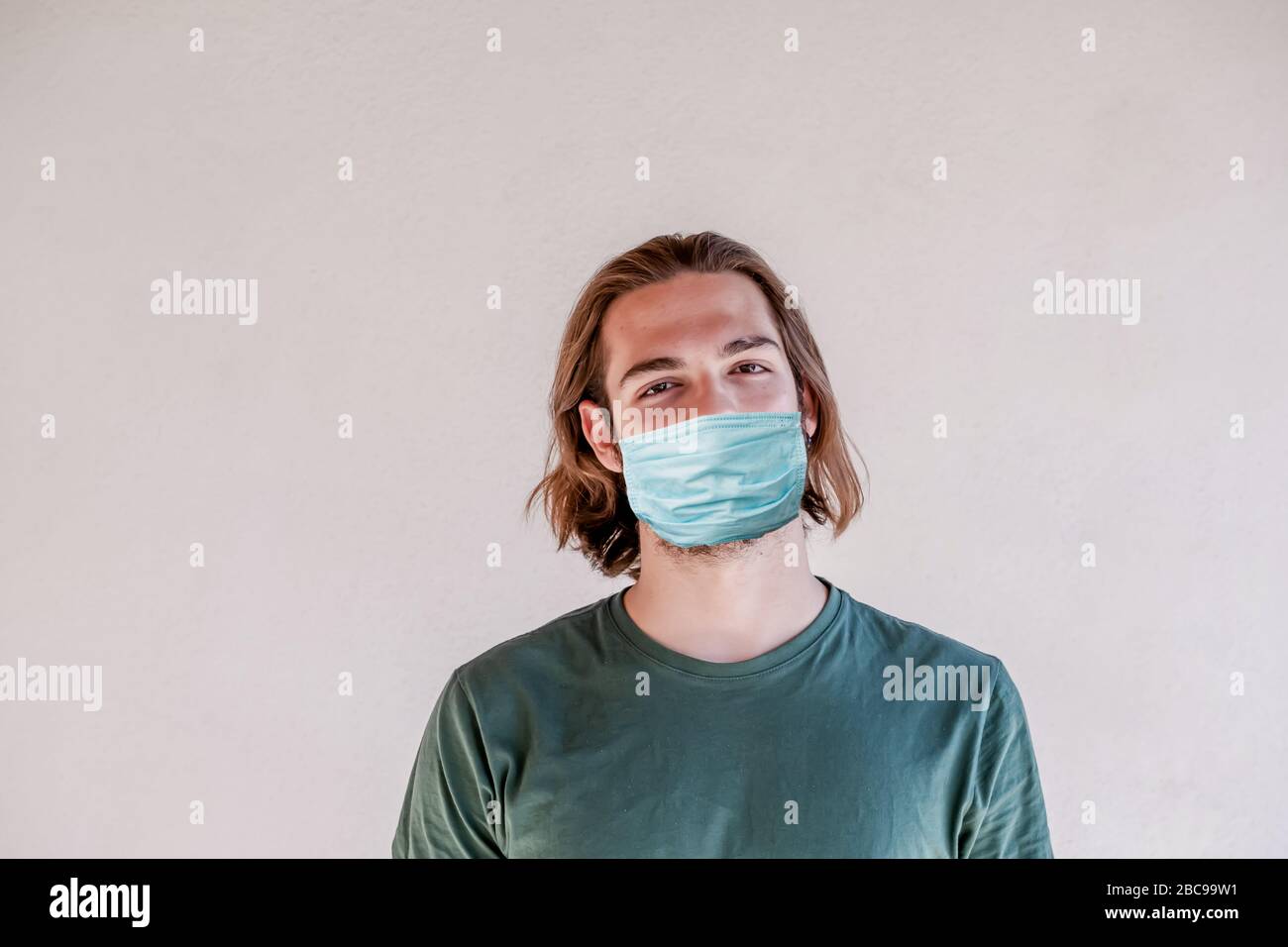 Giovane ragazzo che indossa maschera chirurgica viso, lungo capelli uomo prendere una maschera viso per coronavirus o COVID-19 epidemia Foto Stock