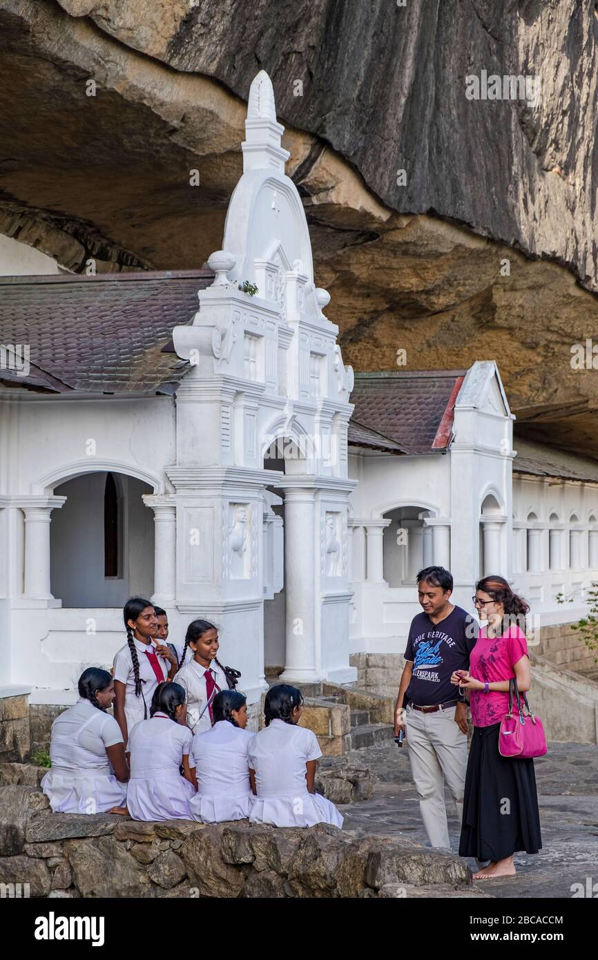Un gruppo di ragazze scolastiche parla con i turisti di fronte ai templi rupestri di Dembulla, Sri Lanka Foto Stock
