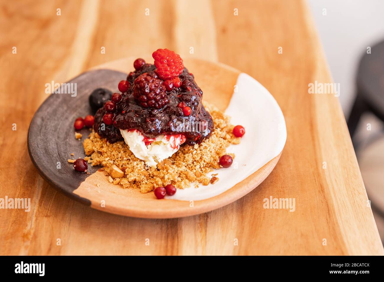 Cheesecake semi-congelato alla frutti di bosco (mora e lampone) con crumble di mandorle schiacciate. Servito in piatti in ceramica in tre colori. Foto Stock