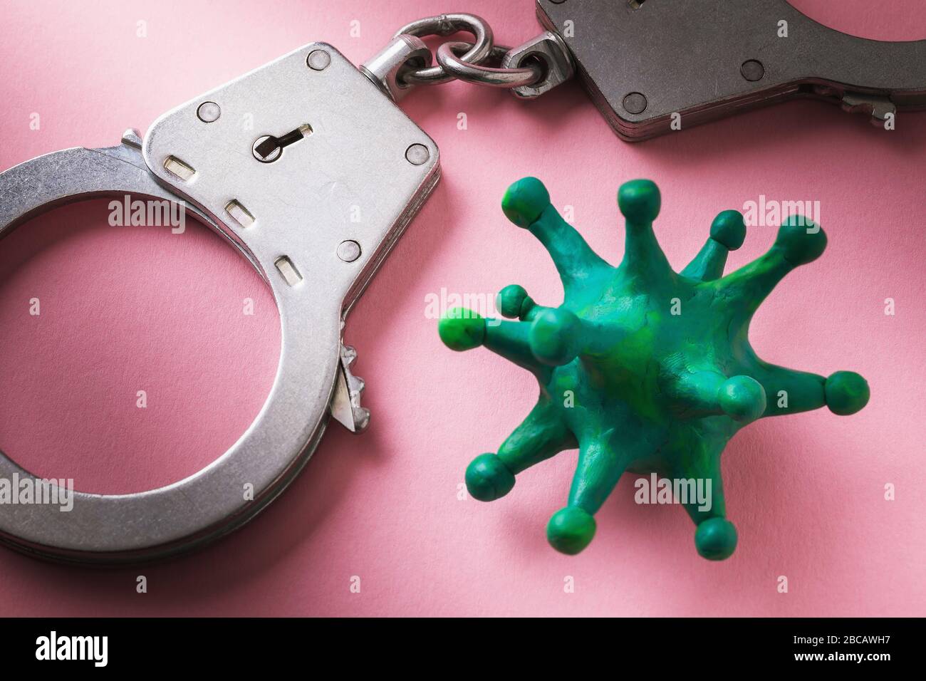 Manette e coronavirus su sfondo rosa. Concetto sul tema della punizione per la violazione di auto-isolamento in un covid-19 pandemico Foto Stock