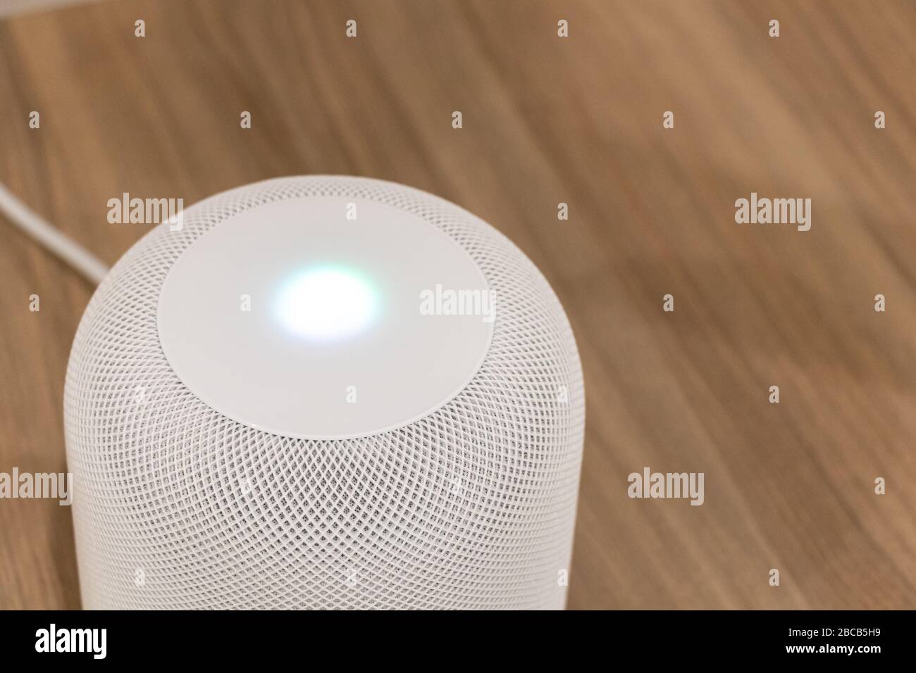 Apple HomePod bianco su un tavolo con la luce Siri accesa sulla parte superiore. Foto Stock