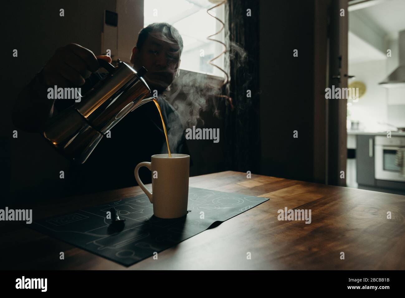 Un uomo che tiene una moka in pentola e versa il caffè. Caffè da primo piano isolato in spazi bui. Foto Stock