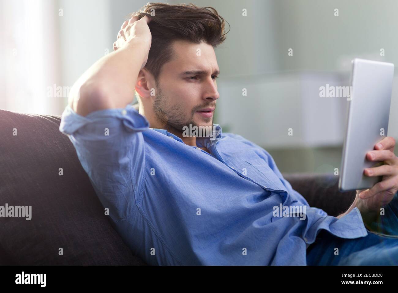 Uomo seduto sul divano con la tavoletta digitale Foto Stock
