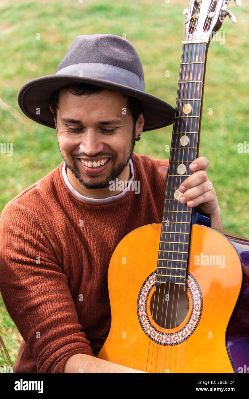 Il giovane ispanico suona la chitarra seduto in un parco della città Foto Stock