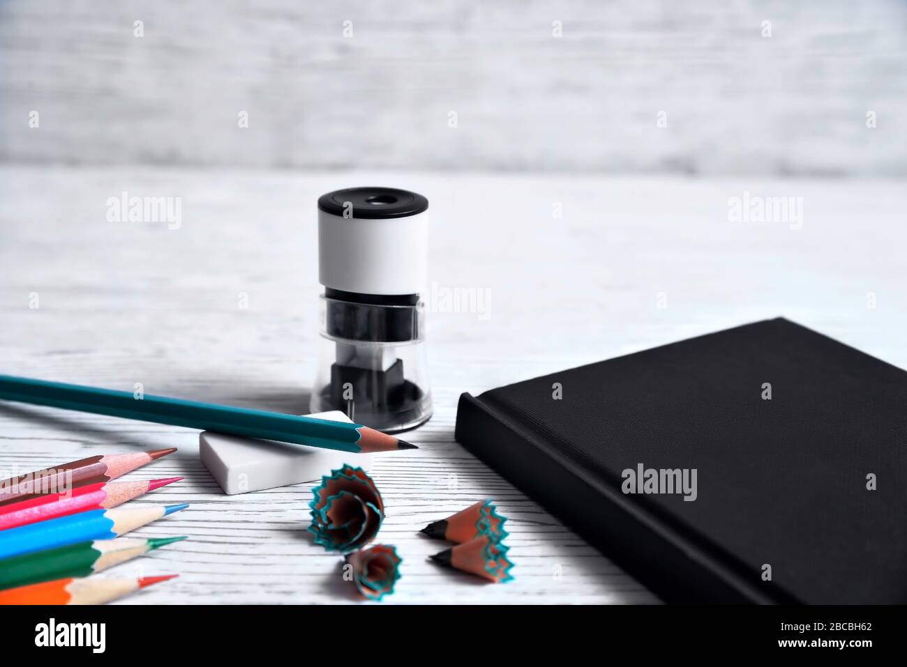 Matite, blocco note, affilatrice, cancellatrice e trucioli da matite su sfondo grigio non uniforme Foto Stock