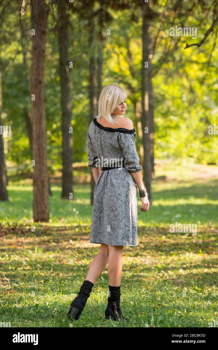 Ritratto di stile di moda di bella donna bionda bella posa con la schiena  girata e guardando sopra la spalla destra in estate verde parco che indossa  il lon Foto stock 