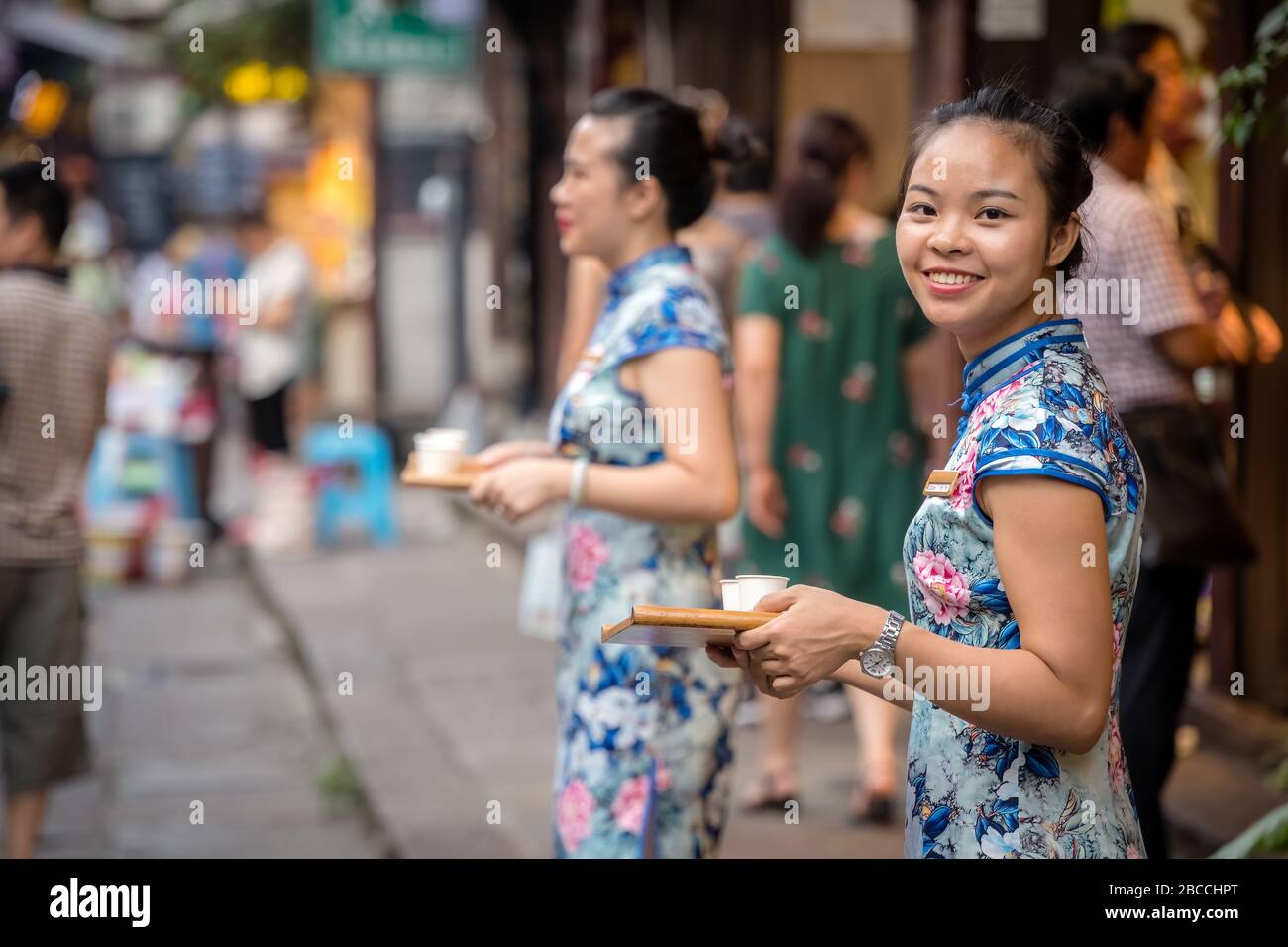 Chongqing, Cina - Agosto 2019 : bella donna cinese in piedi di fronte ad una bancarella di cibo in ci Qi Kou antica città di Chongqing e dare via sam Foto Stock