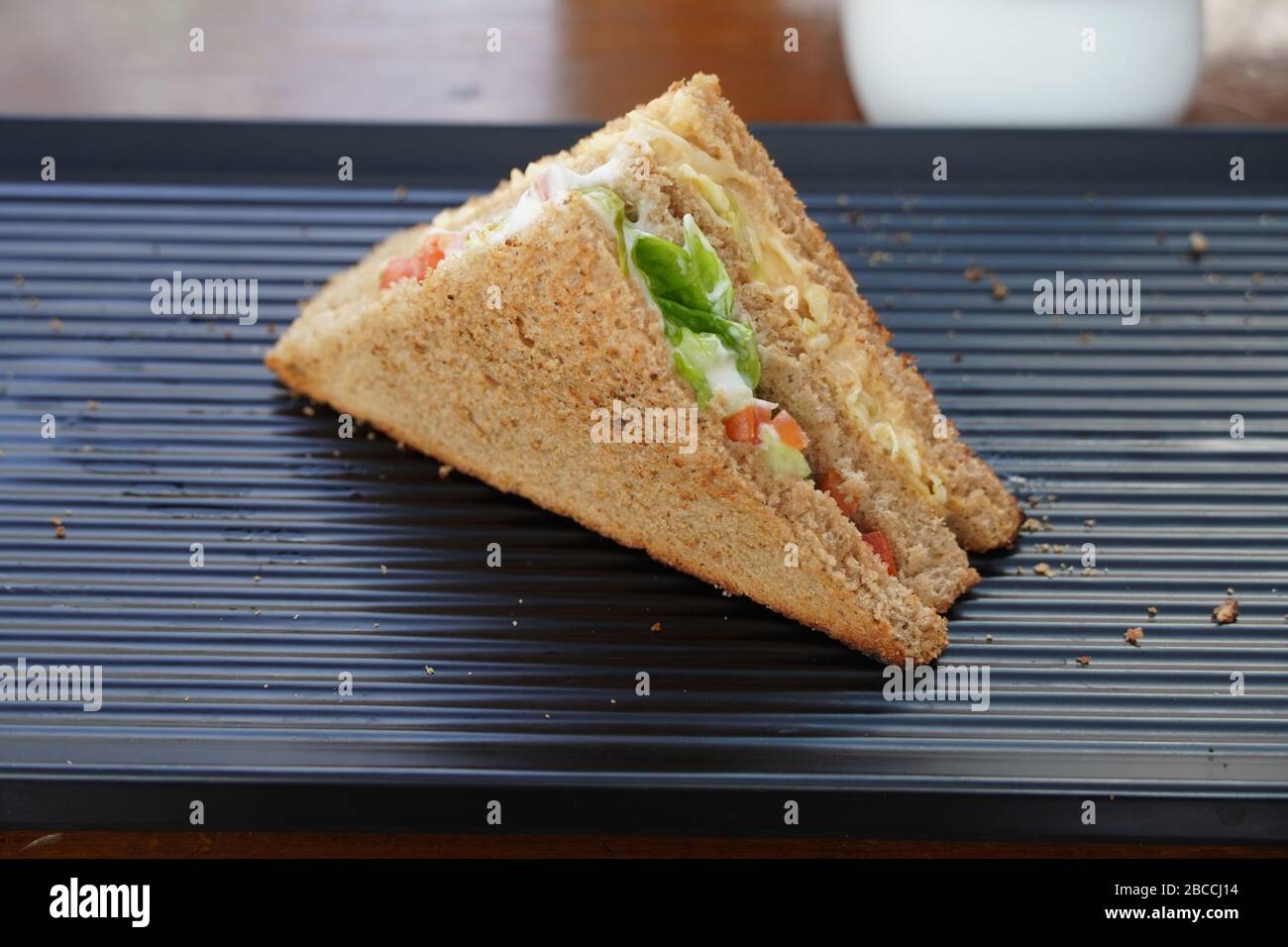 Un unico sandwich di tonno sul piatto da portata nero. Un Club Sandwich con pollo, prosciutto, formaggio, pomodori, cetrioli, pancetta, lattuga, erbe e brea tostata Foto Stock