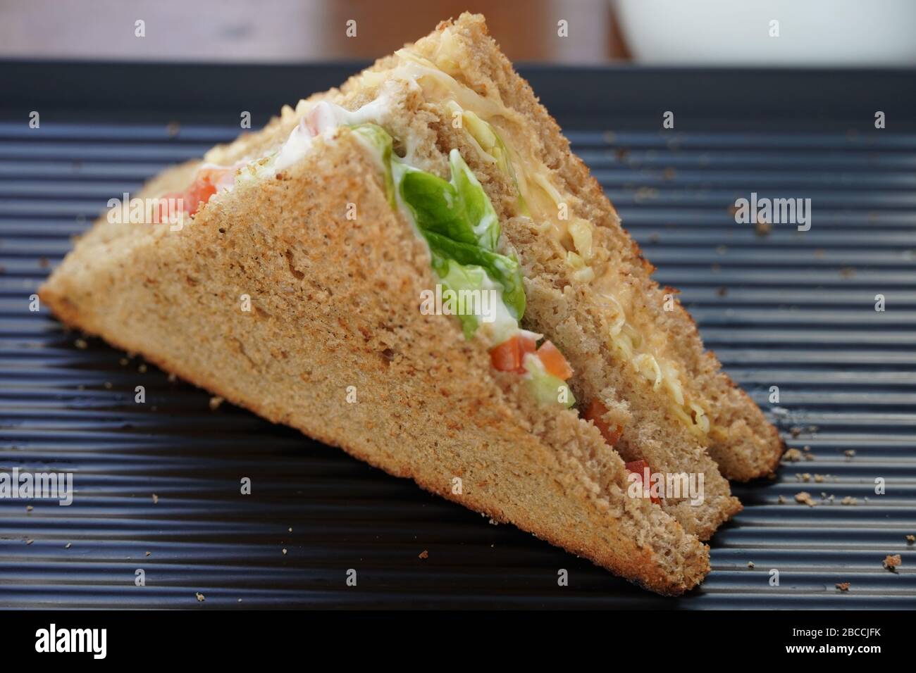 Un unico sandwich di tonno sul piatto da portata nero. Un Club Sandwich con pollo, prosciutto, formaggio, pomodori, cetrioli, pancetta, lattuga, erbe e brea tostata Foto Stock