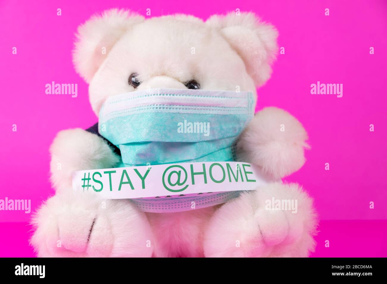 Rimani a casa e Coronavirus COVID-19 concetti. Simpatico orso giocattolo che indossa una maschera medica protettiva per bambini isolata su sfondo rosa. Foto Stock