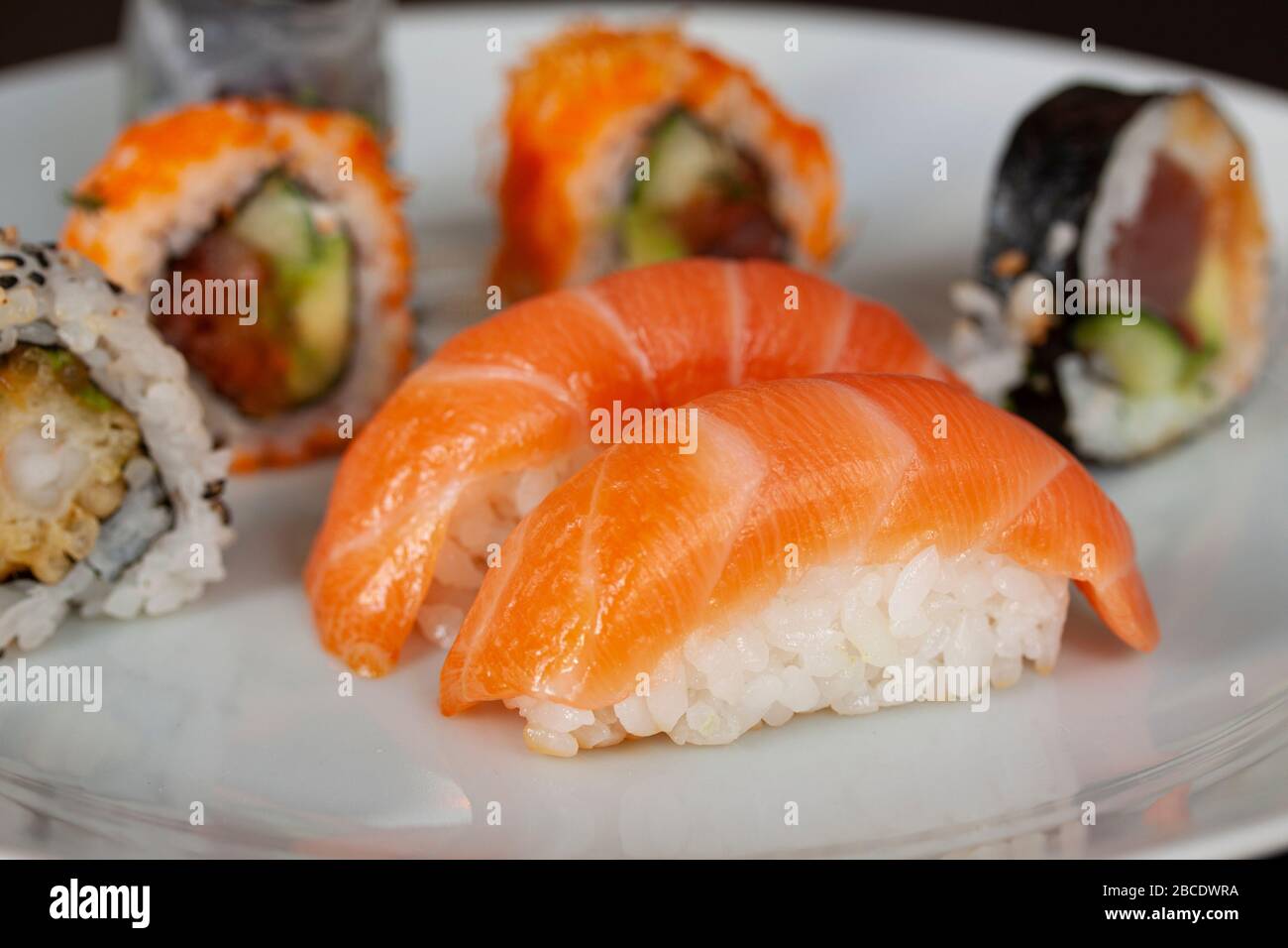 Menù di sushi con panini di salmone, riso e tonno su un piatto con fondo nero. Cucina giapponese. Primo piano con messa a fuoco selettiva. Foto Stock