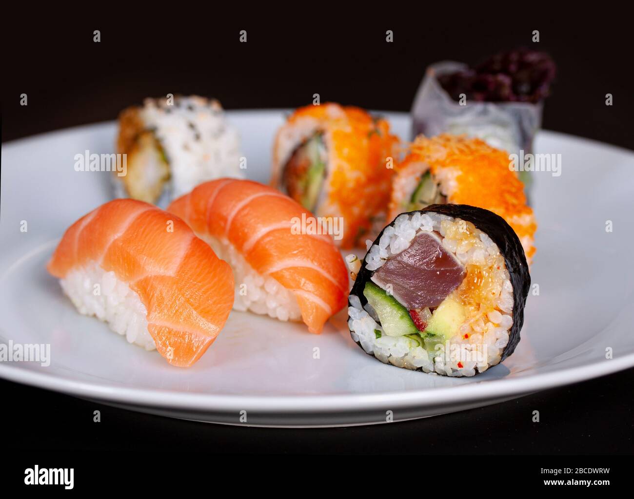 Menù di sushi con panini di salmone, riso e tonno su un piatto con fondo  nero. Cucina giapponese. Primo piano con messa a fuoco selettiva Foto stock  - Alamy