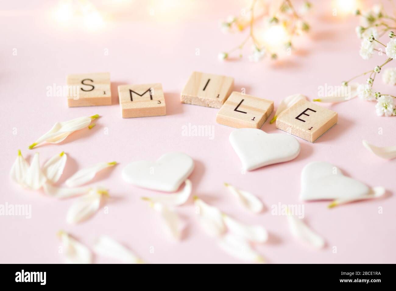 Sorriso di parola in piastrelle di legno lettera contro un morbido sfondo rosa - concetto di vita ferma Foto Stock