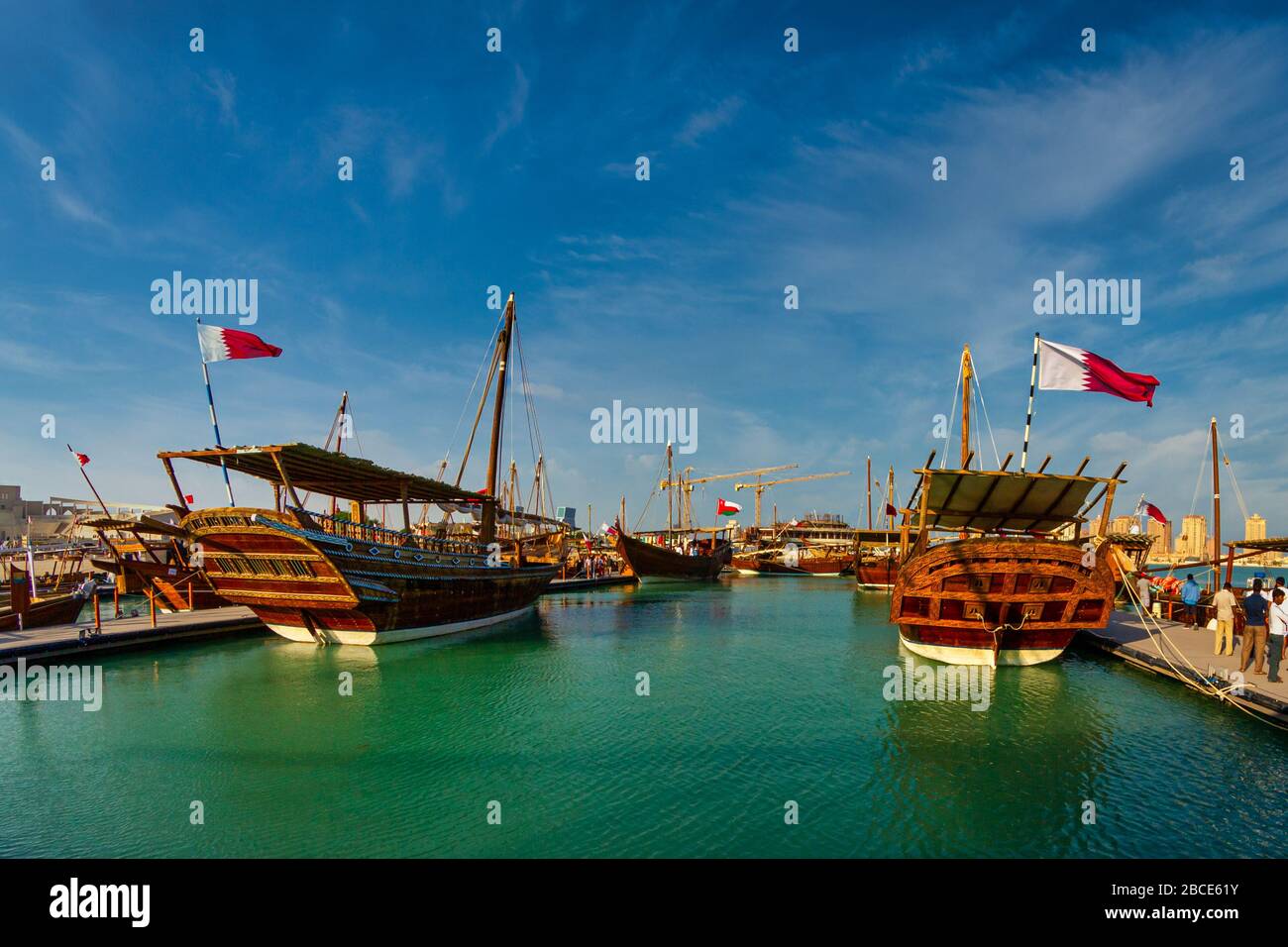 Tradizionali barche in legno (dhows) a Katara spiaggia Qatar vista luce del giorno con bandiera Qatar e nuvole nel cielo Foto Stock