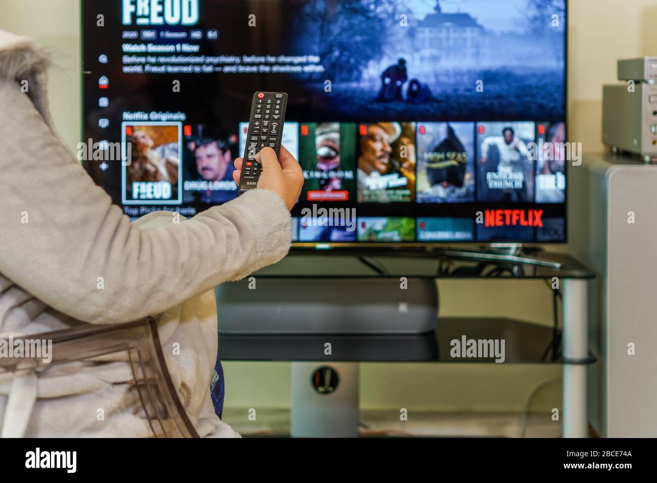TV watching Netflix streaming Service VoD c.. Donna in casa con telecomando, visualizzazione su una pagina online del provider di servizi di streaming su grande schermo. Foto Stock