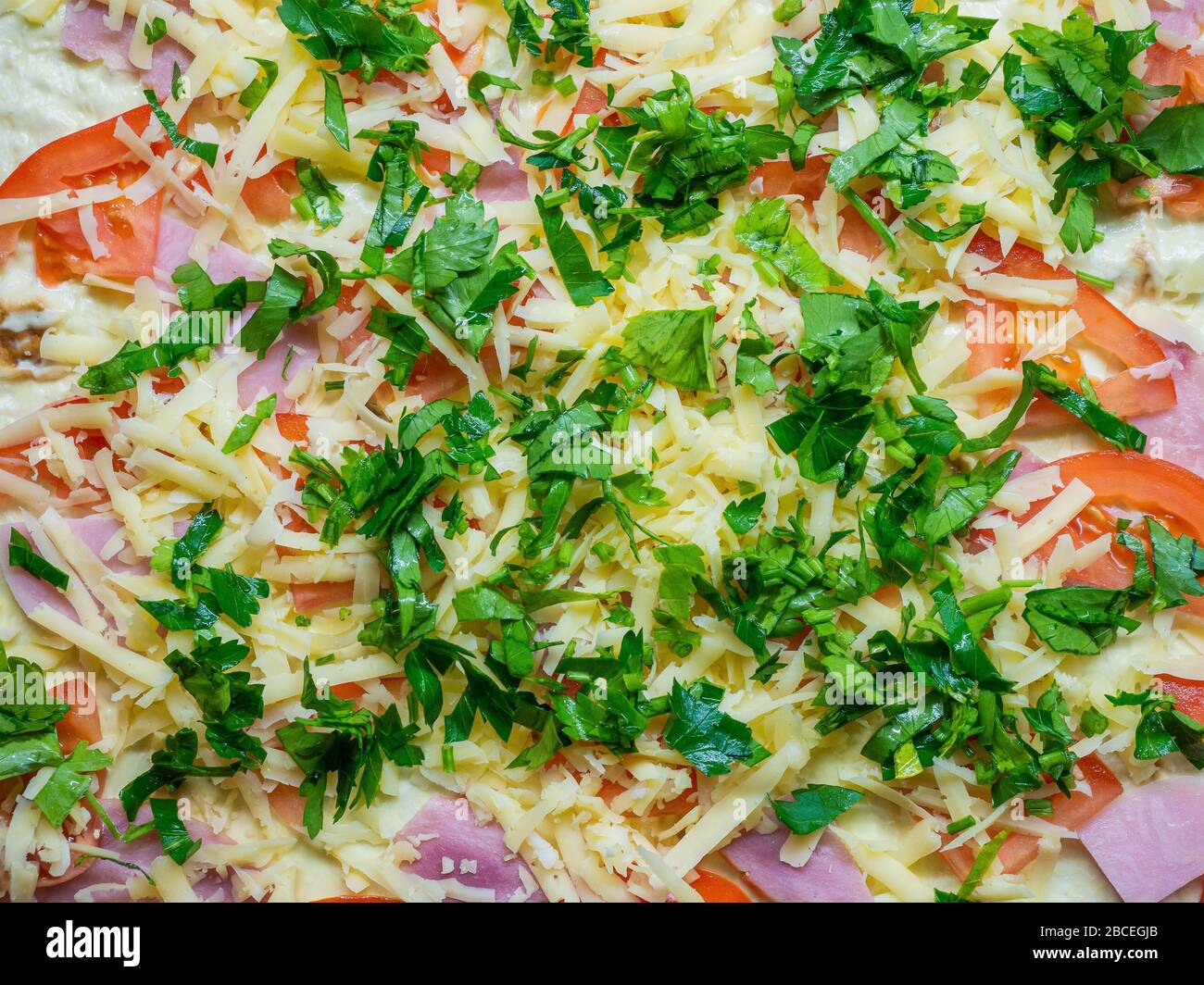 Preparato per la cottura con fette di prosciutto, pomodori, formaggio grattugiato e verdure tritate Foto Stock