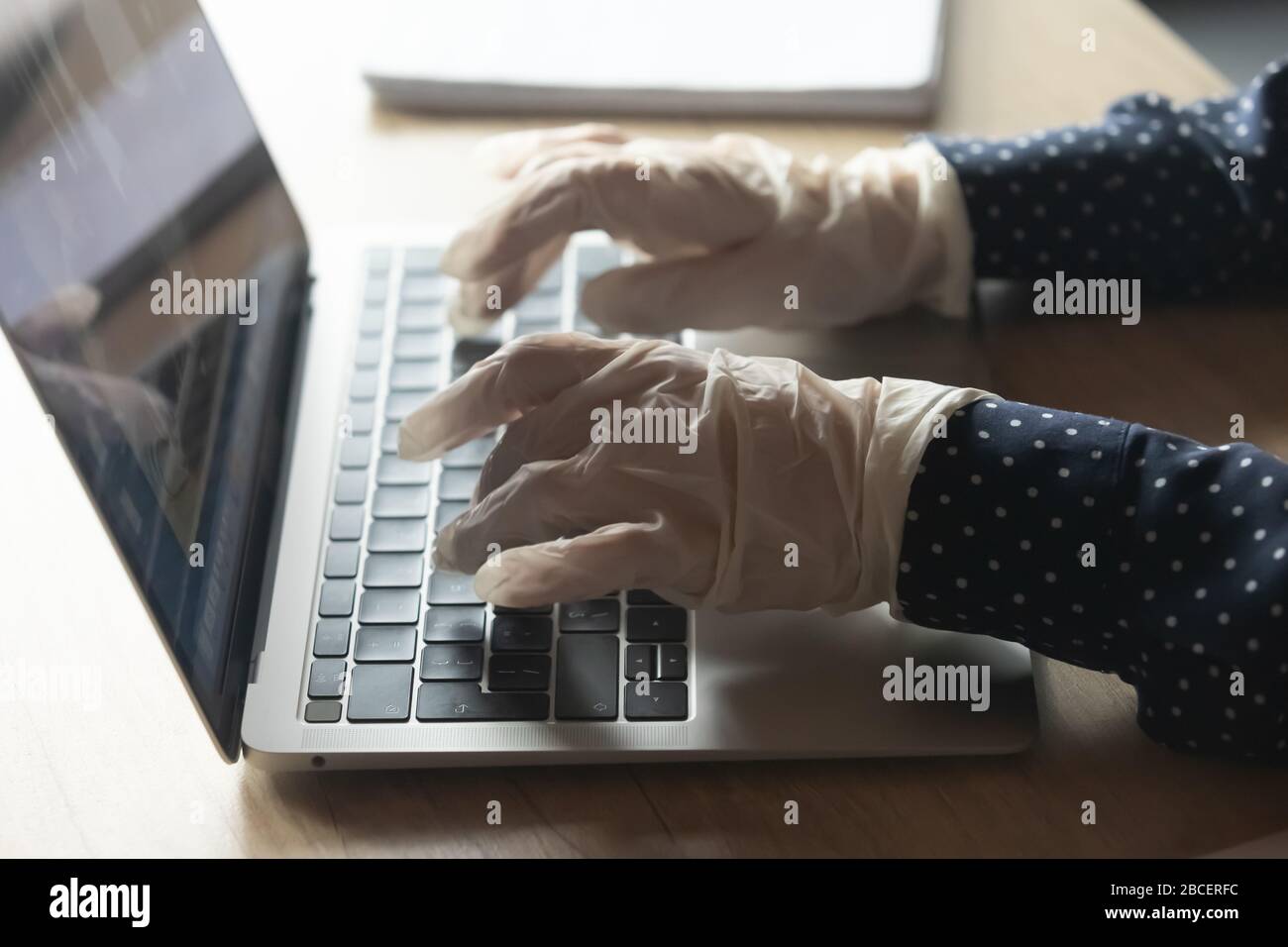 Le mani femminili nei guanti protettivi scrivano il messaggio sulla tastiera del computer. Foto Stock