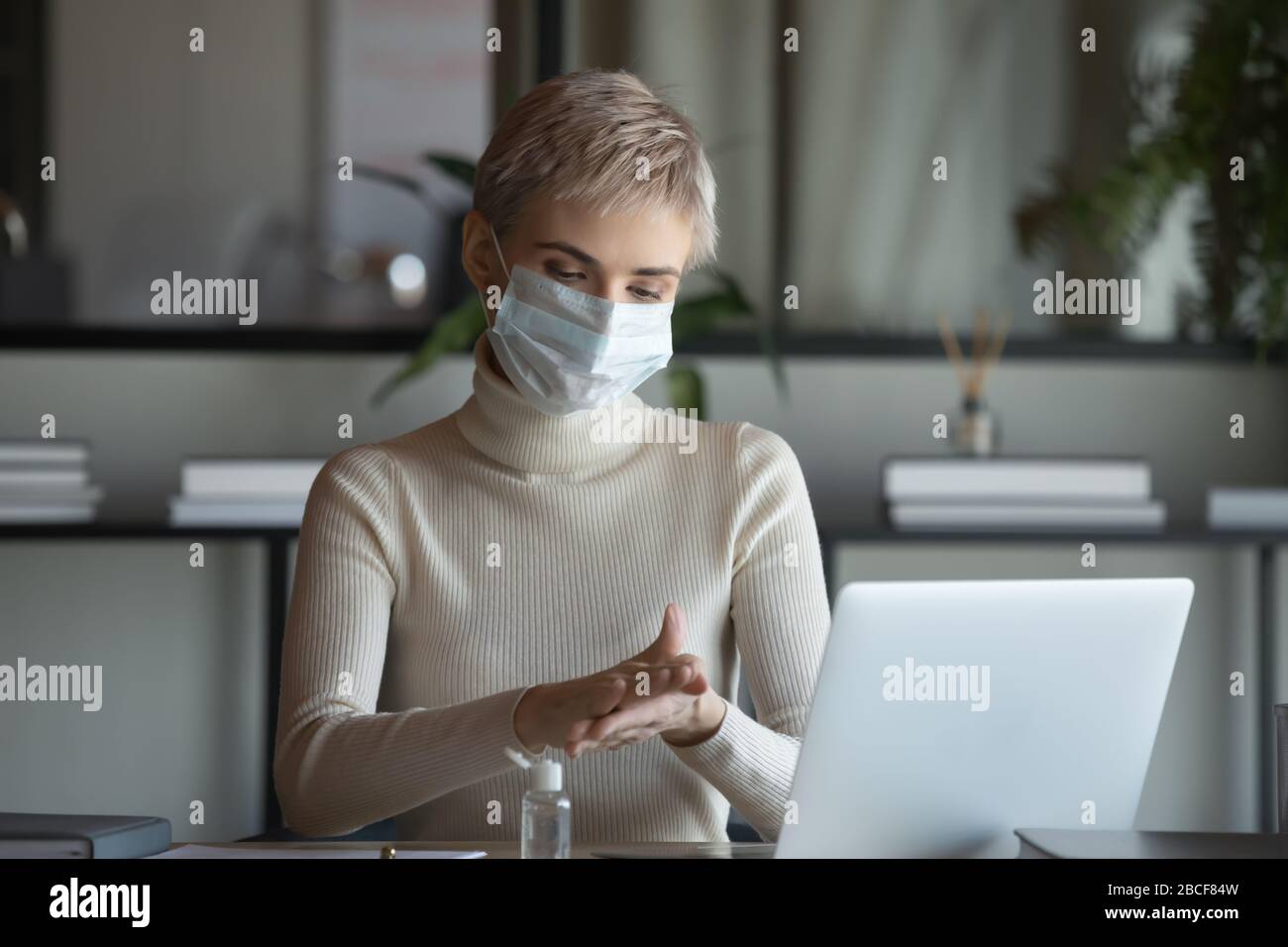 30s donna d'affari in maschera protettiva medico disinfettante mani. Foto Stock