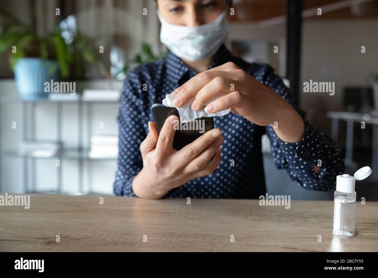 Giovane donna cauto che indossa una maschera medica, uccidendo i batteri sullo smartphone. Foto Stock