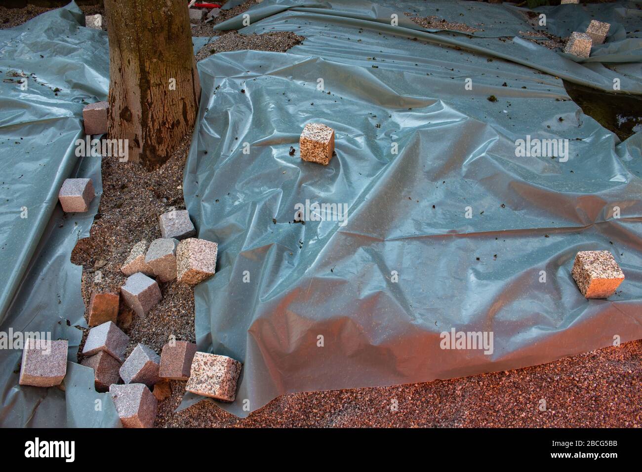 I ciottoli pesano un foglio di plastica che copre un cantiere di pavimentazione Foto Stock