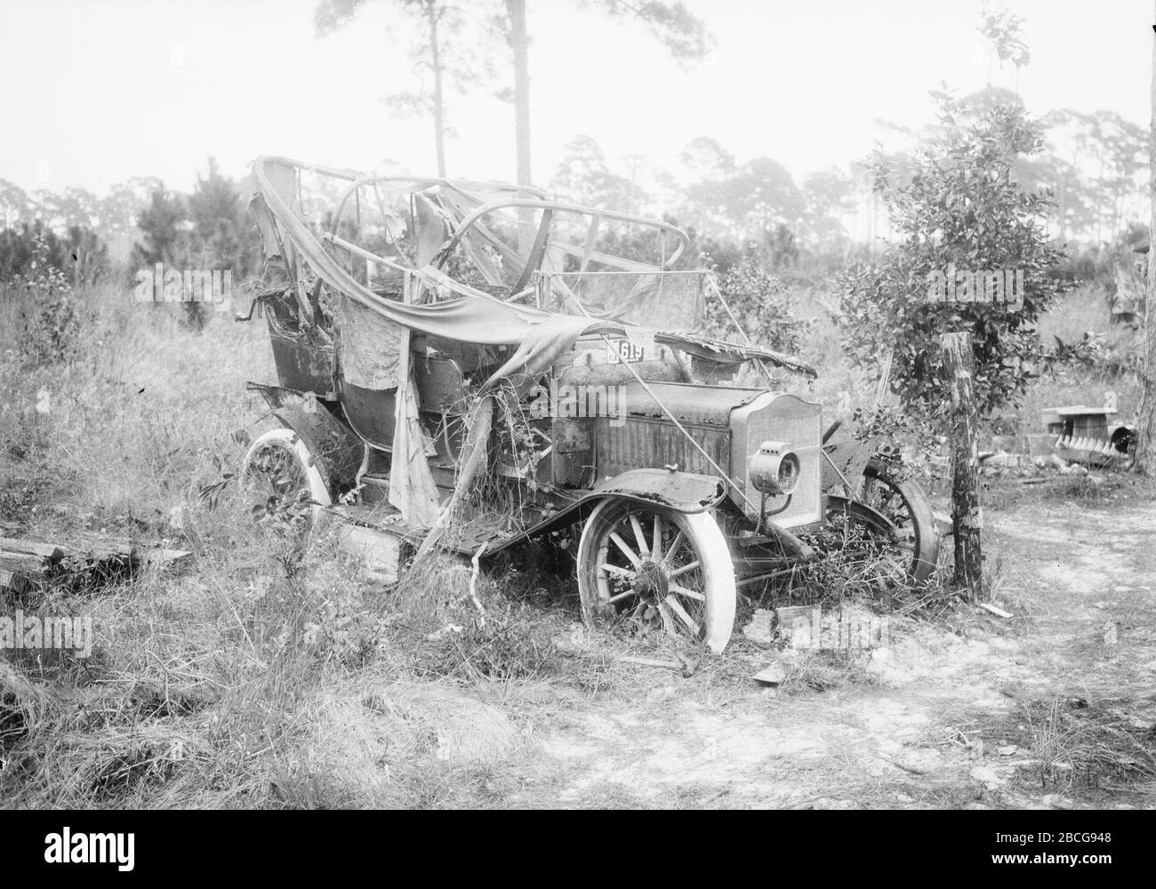 Un'auto distrutta in un campo d'erba, Florida, 1920. (Foto di Burton Holmes) Foto Stock