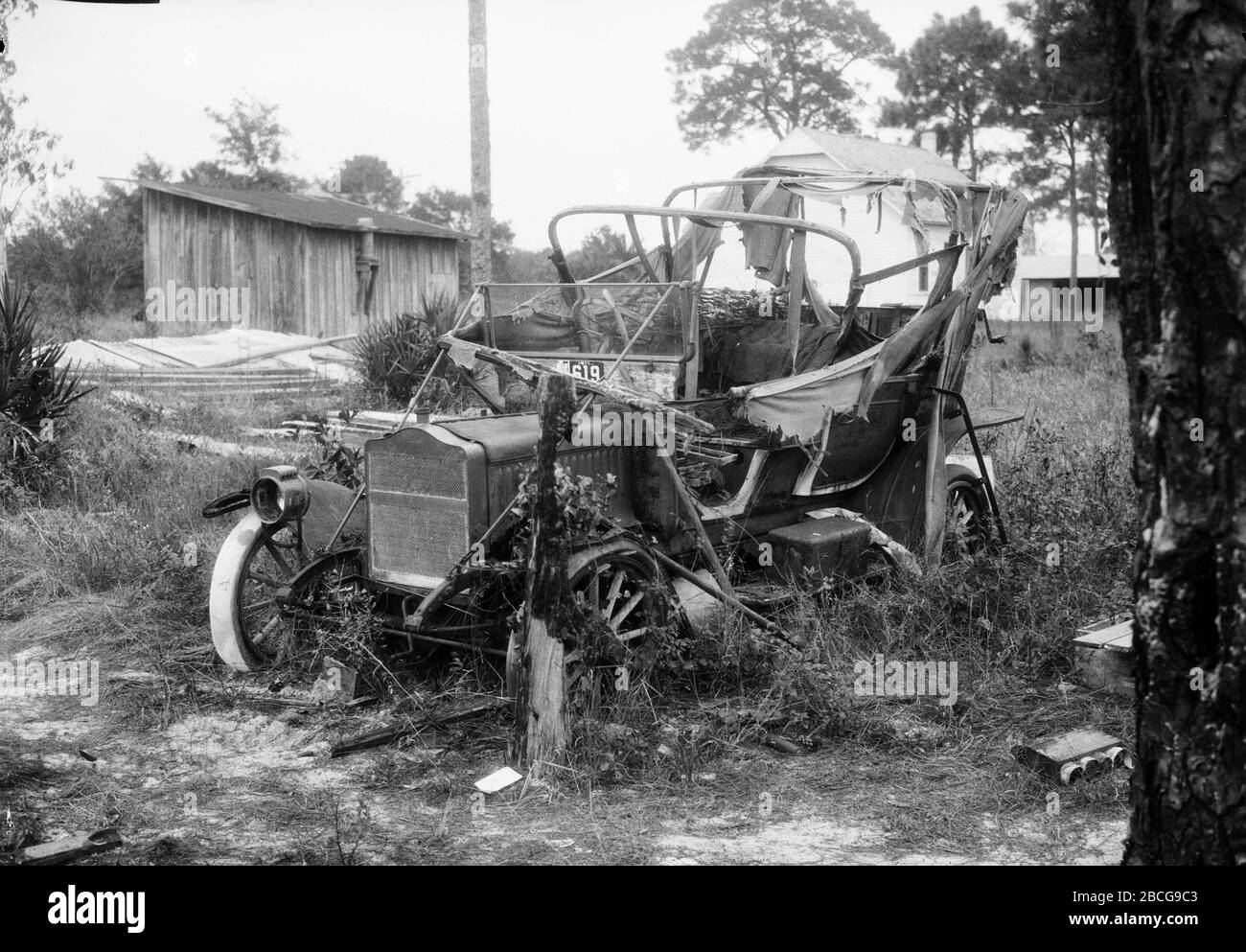 Un'auto distrutta in un campo d'erba, Florida, 1920. (Foto di Burton Holmes) Foto Stock