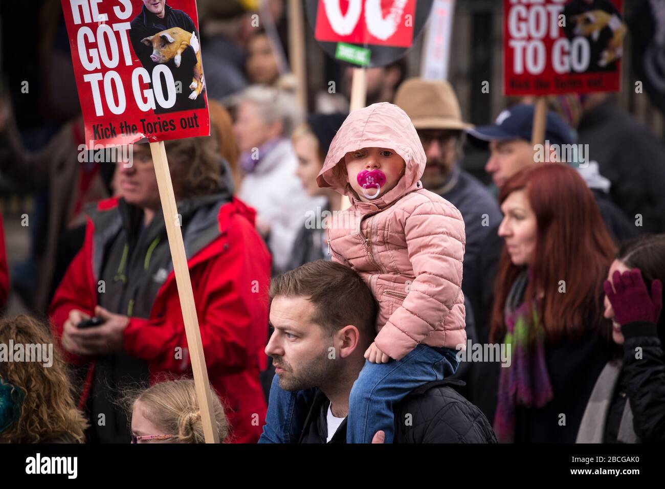 Bambino con un manichino in bocca e seduto sulle spalle di un adulto durante una manifestazione anti-austerità a Londra Foto Stock