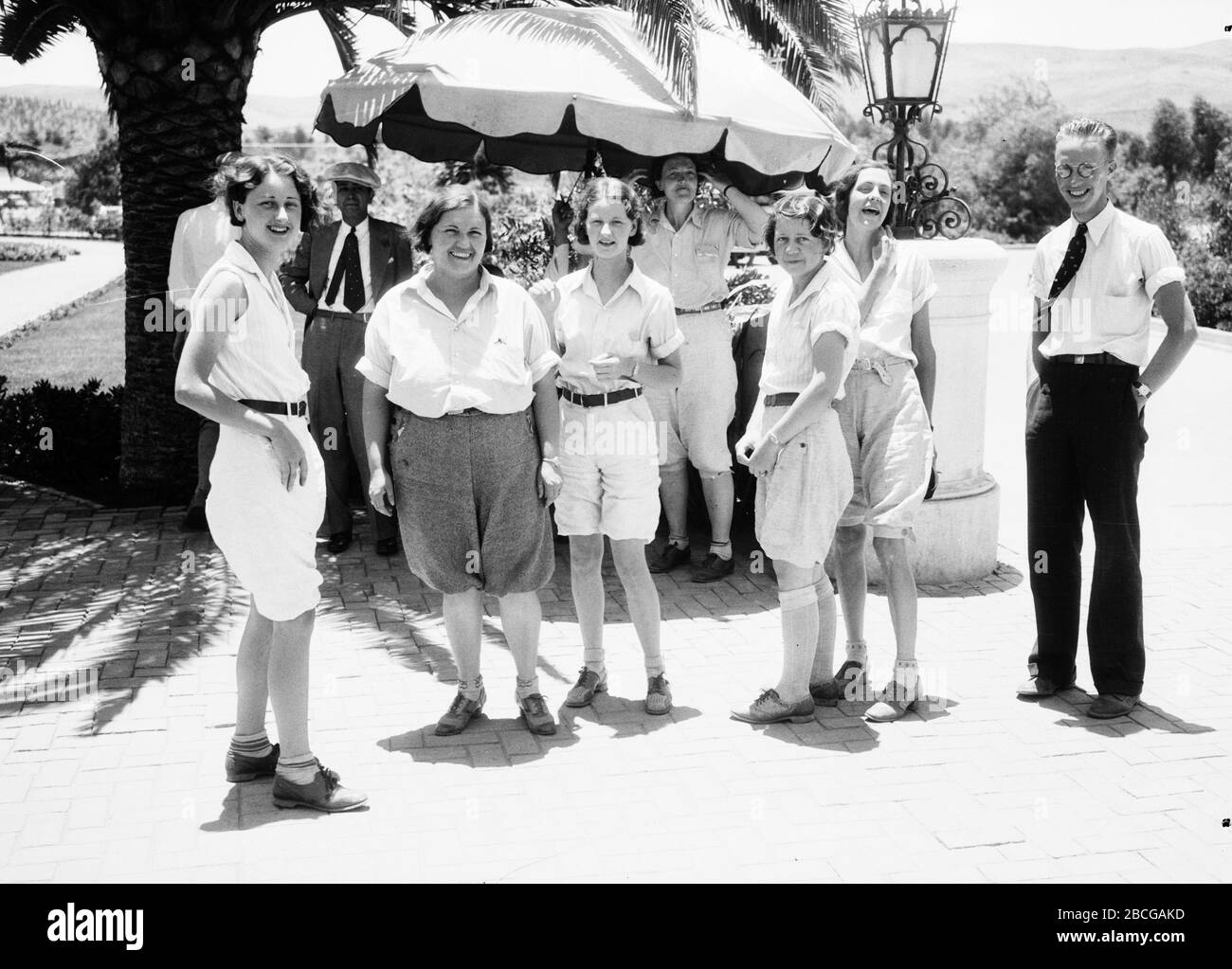 Un gruppo di turisti femminili si trovano all'esterno con uomini nelle vicinanze, Hotel Agua Caliente, Tijuana, Messico, alla fine degli anni '20. Fotografia di Burton Holmes. Foto Stock