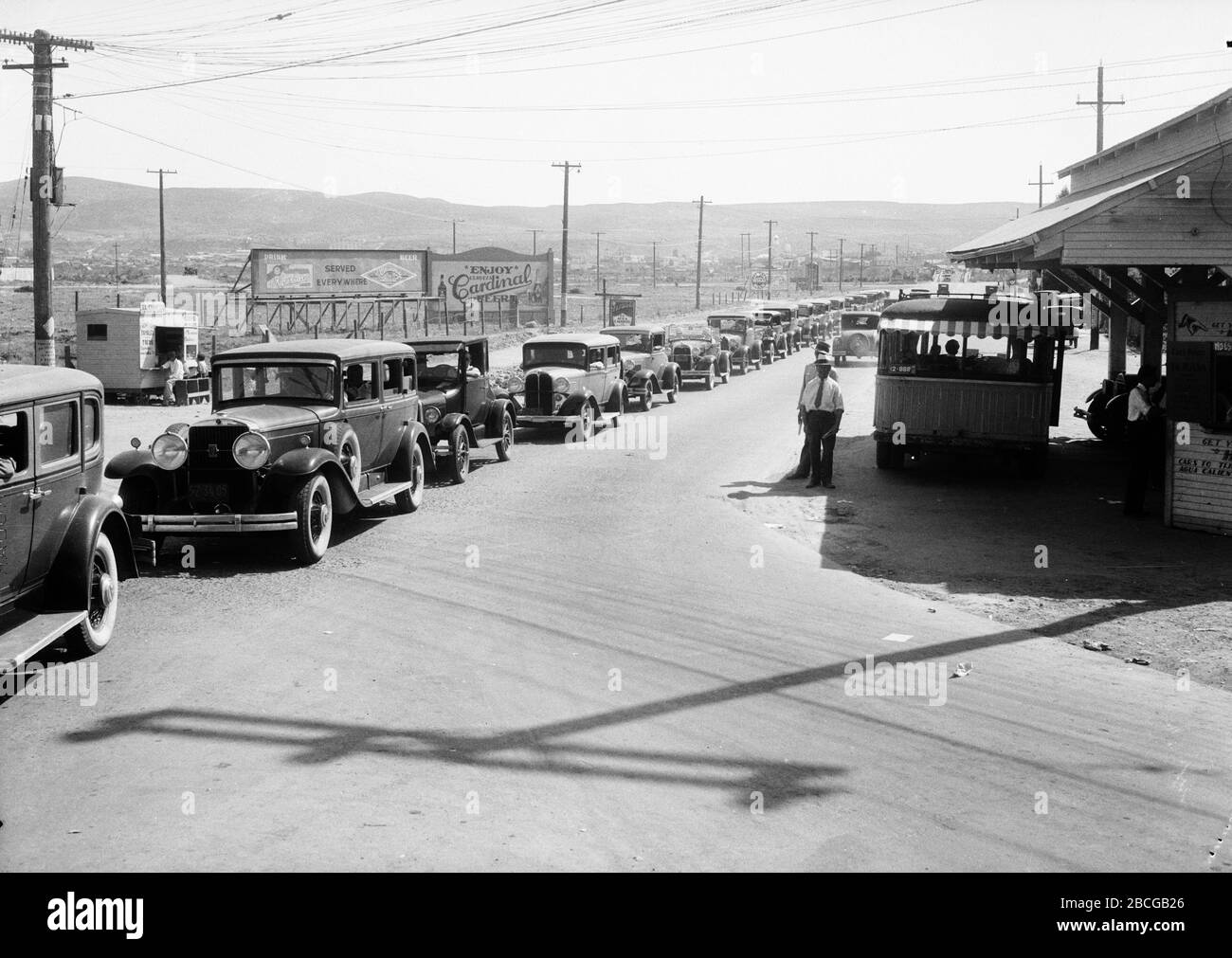 Una lunga serie di auto aspetta di sdoganare le dogane e attraversa il confine tra Stati Uniti e Messico a Tijuana, Messico e San Ysidro, California, anni venti. Fotografia di Burton Holmes. Foto Stock