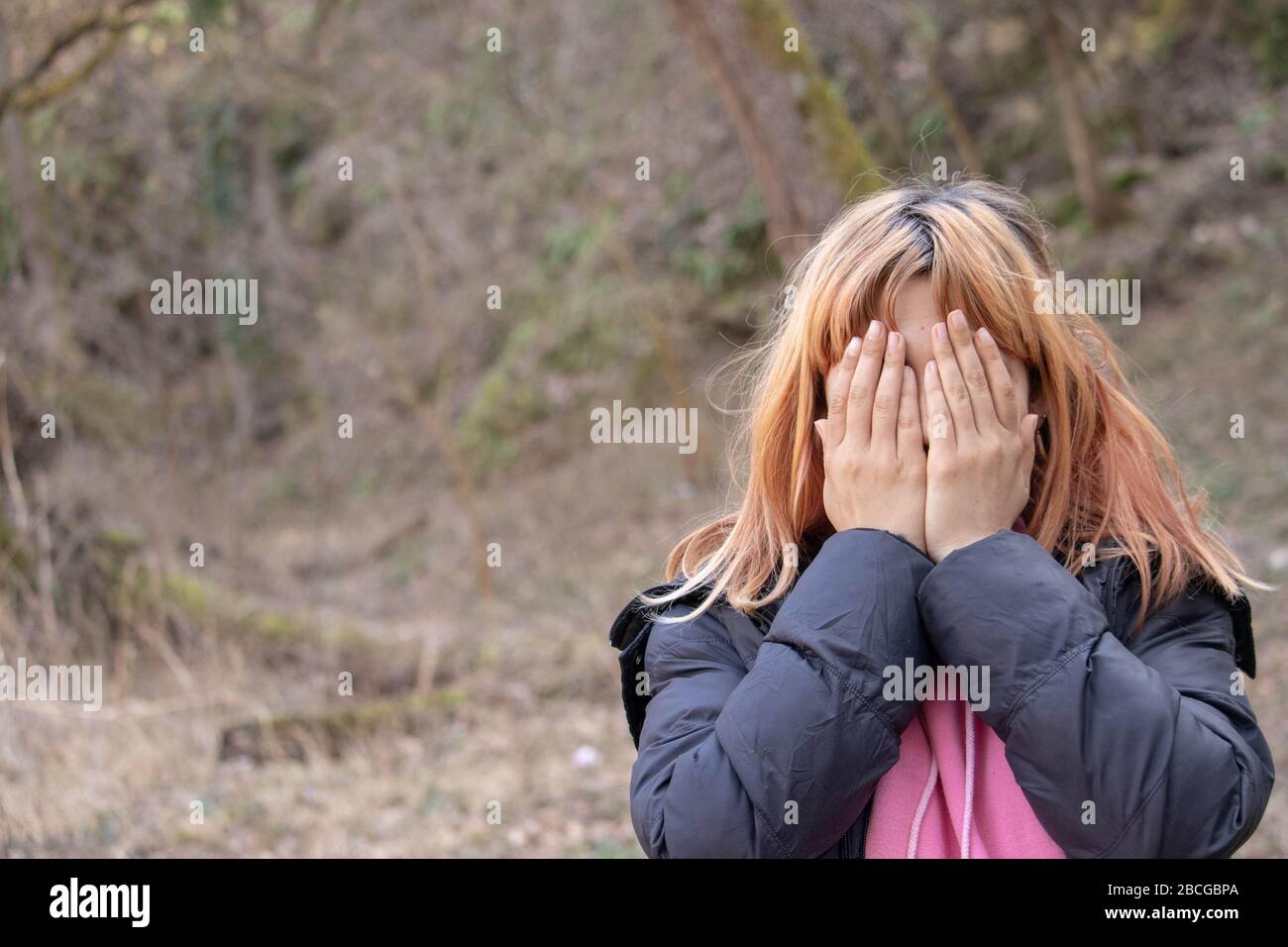 Ragazza che piange in natura. Persona in agonia che tiene le mani sul suo viso. Donna giovane depressa in camicia che ha scoppiato di rabbia e tristezza in natura. Mani Foto Stock