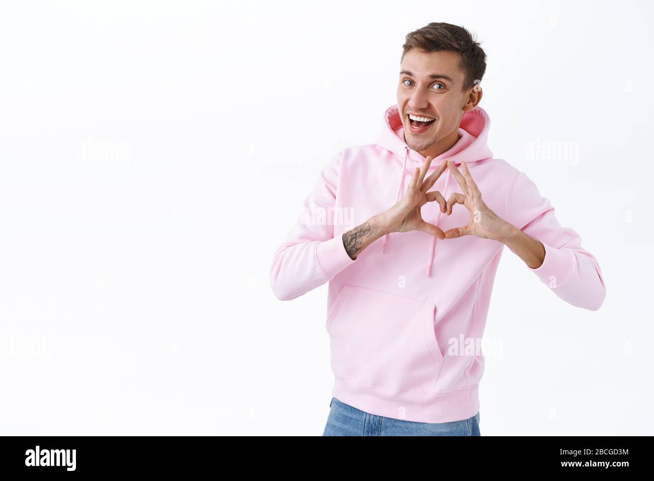Allegro uomo biondo romantico esprimere la sua simpatia, complimentarsi con l'amante con anniversario, mostrare segno di cuore come confessa in amore e sentimenti teneri, sorridendo Foto Stock