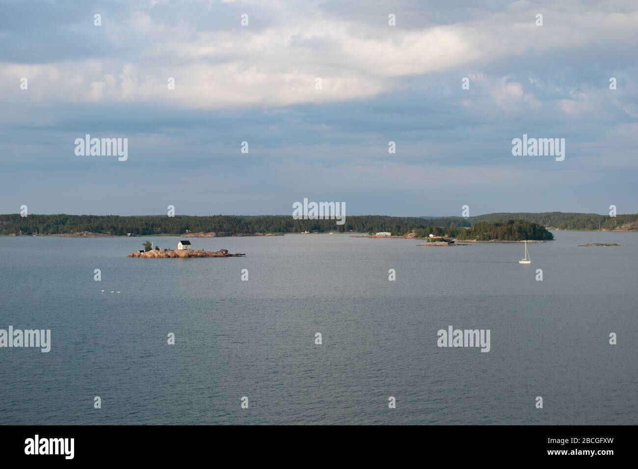 Vista panoramica di un piccolo cottage su una piccola isola rocciosa dell'arcipelago di Turku con una barca a vela che passa attraverso la baia. Foto Stock