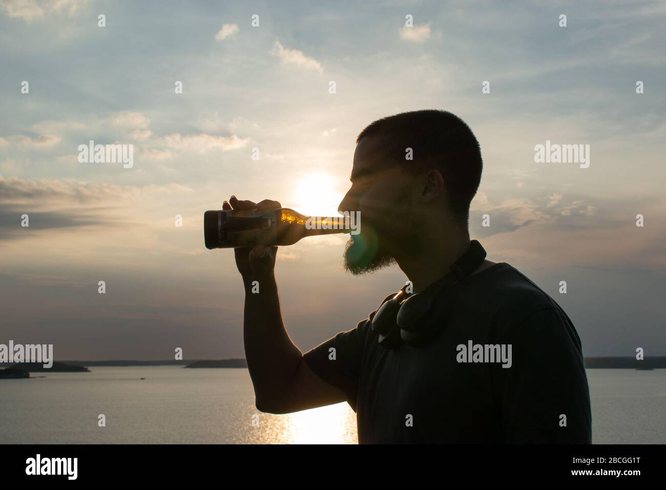 Ritratto ricco di contrasto di un uomo che beve una birra davanti al sole a metà estate nell'arcipelago di Turku. Foto Stock