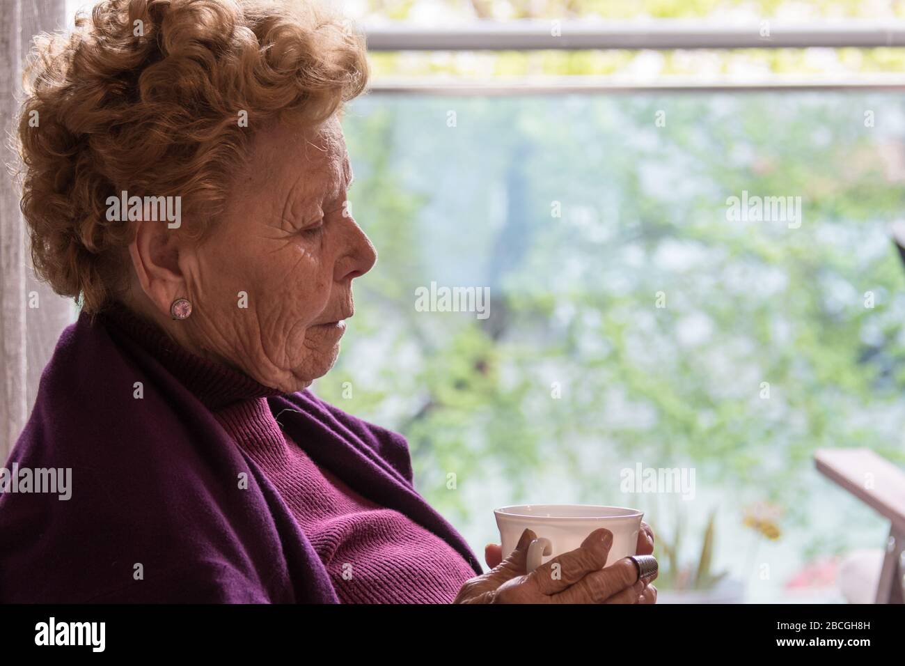 Donna anziana seduta accanto alla finestra Foto Stock