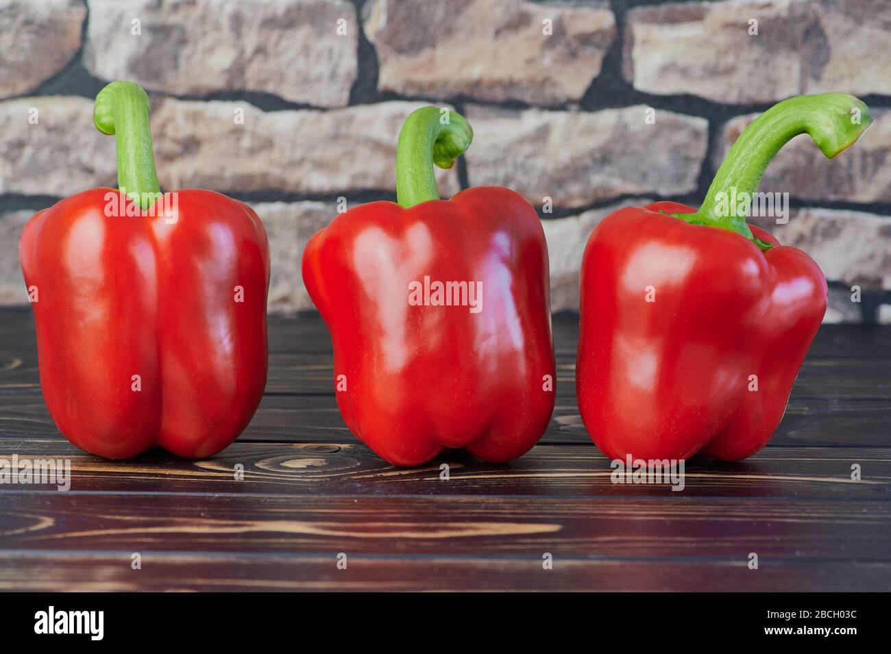 tre peperoni rossi su un tavolo di legno davanti ad una parete sfocata Foto Stock