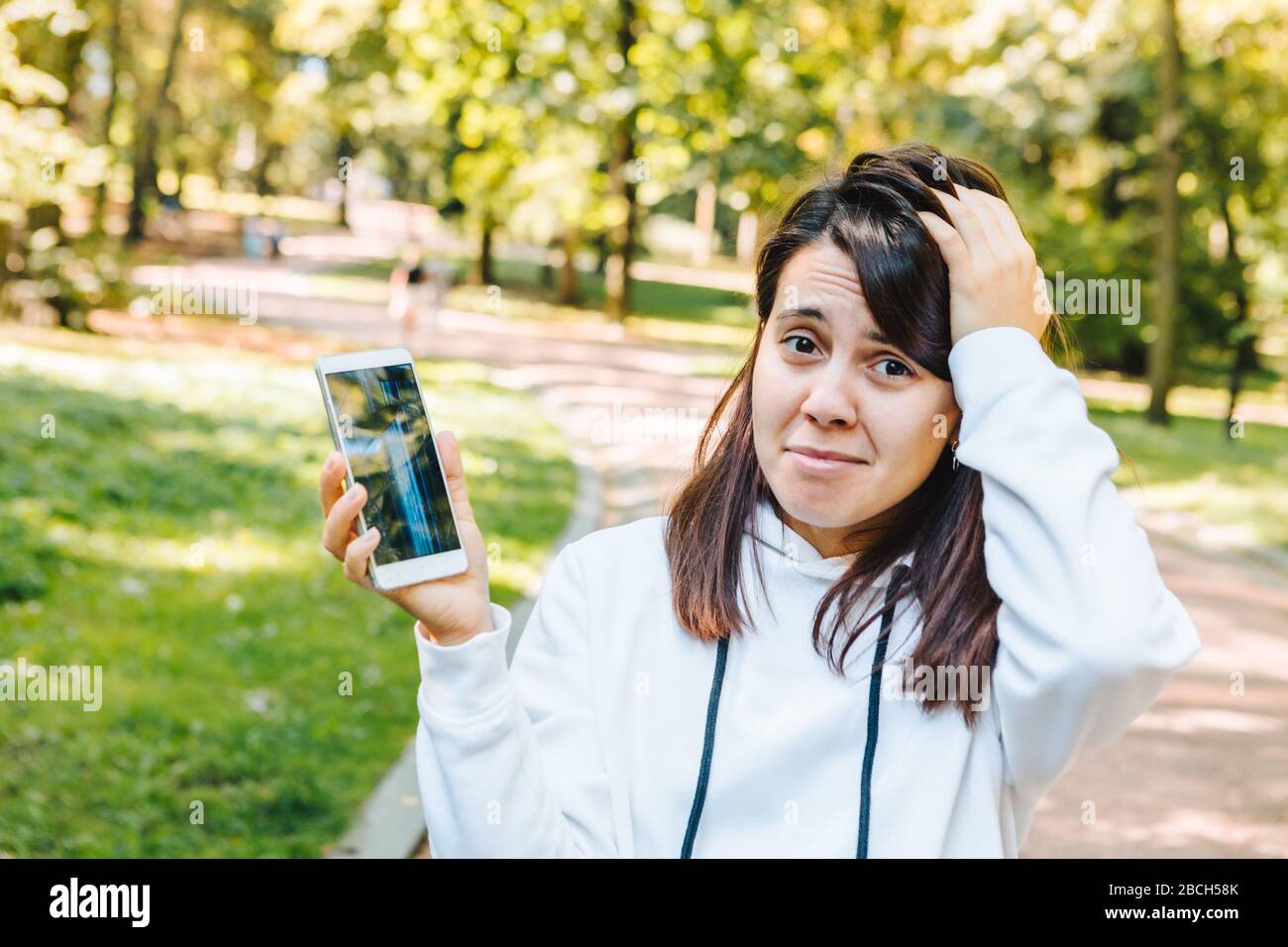 donna triste che mostra schermo mobile rotto dopo caduta Foto Stock