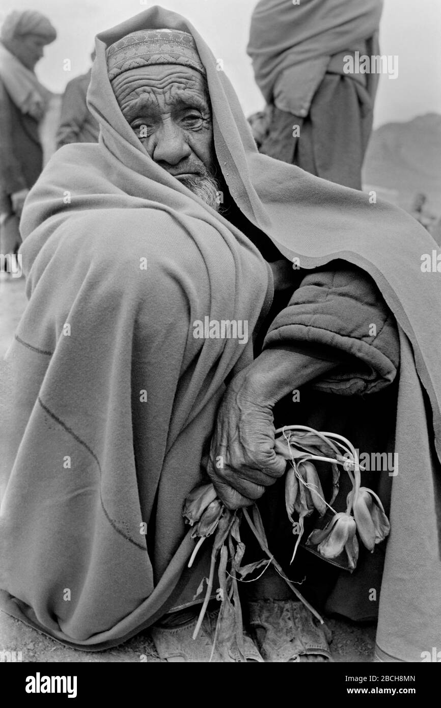 Un uomo afgano anziano tiene un mazzo di tulipani sbiaditi mentre piange al cimitero di suo figlio ucciso nella guerra civile dai combattenti mujahideen afgani dopo i funerali ai terreni funerari di Martyrs Hill il 27 aprile 1989 a Kabul, Afghanistan. Foto Stock