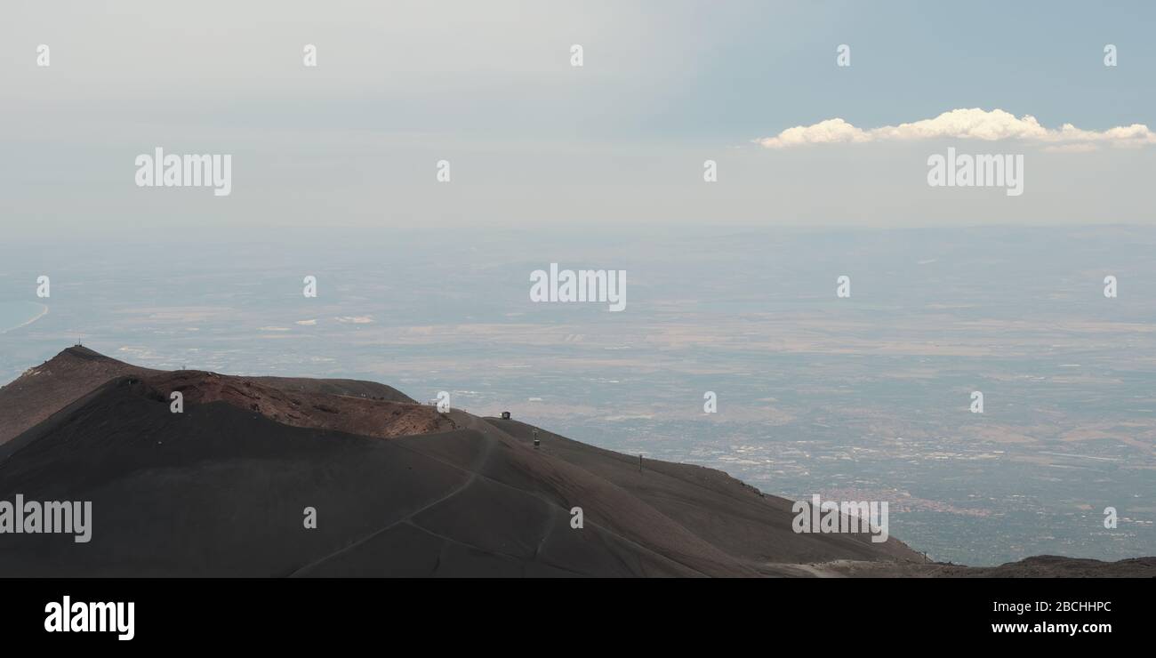Panoramica sul Monte Etna di un vulcano inferiore e le terre lontane con una lunga nuvola solitaria, Sicilia, Italia. Foto Stock