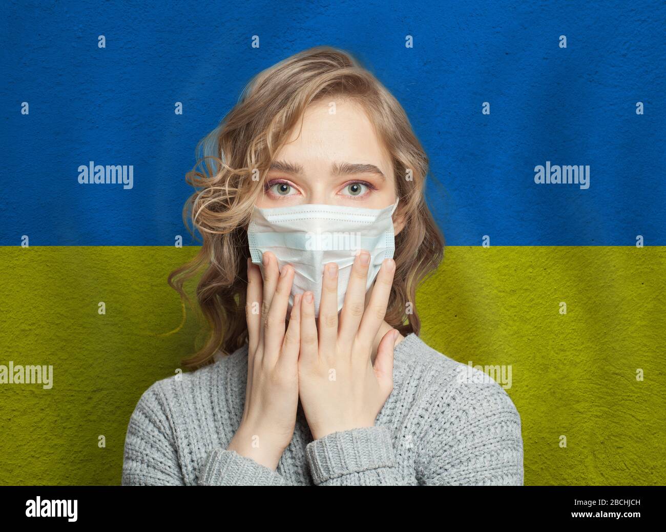 Donna in preda al panico che indossa una maschera facciale sullo sfondo della bandiera Ucraina. Concetto di protezione contro l'epidemia di influenza e i virus Foto Stock