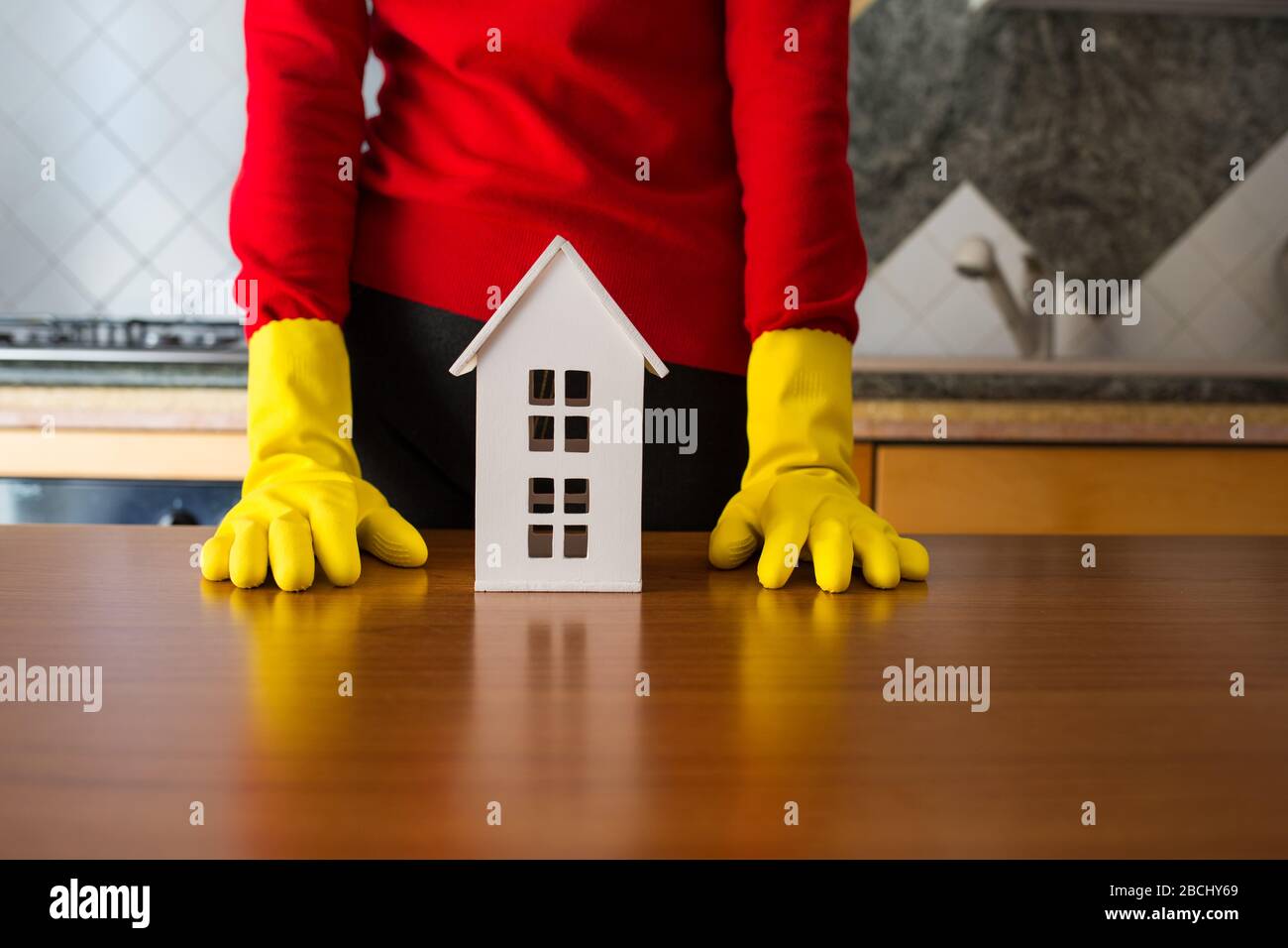 Immagine concettuale di persona con guanti da cucina e una casa modello sopra un tavolo Foto Stock