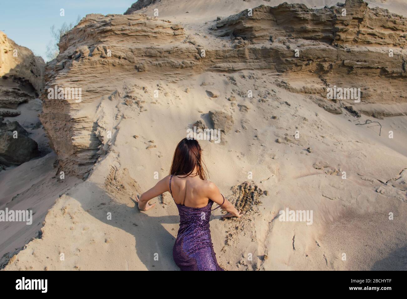 Donna dai capelli castani in abito viola scintillante giace sul pendio di sabbia Foto Stock