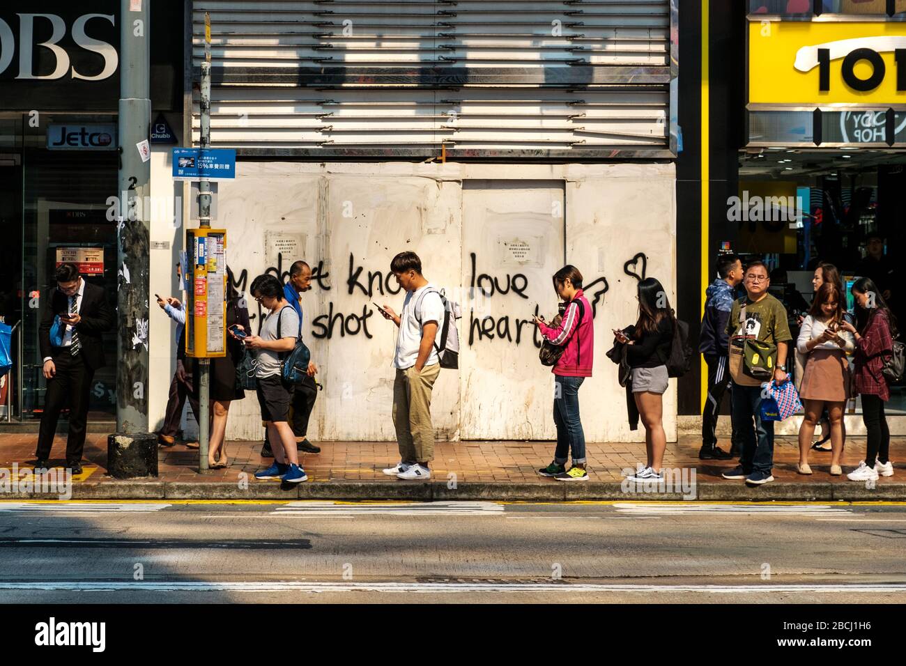 Hong Kong - Novembre 2019: Persone in coda per strada, in attesa di un autobus che cerca un telefono cellulare a Hong Kong Foto Stock