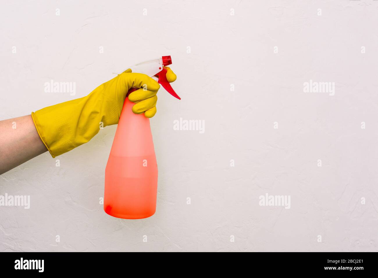 Mano del lavoratore in un guanto giallo con una pistola a spruzzo rossa su sfondo bianco. Protezione contro germi, batteri e virus. Prevenzione delle infezioni d Foto Stock