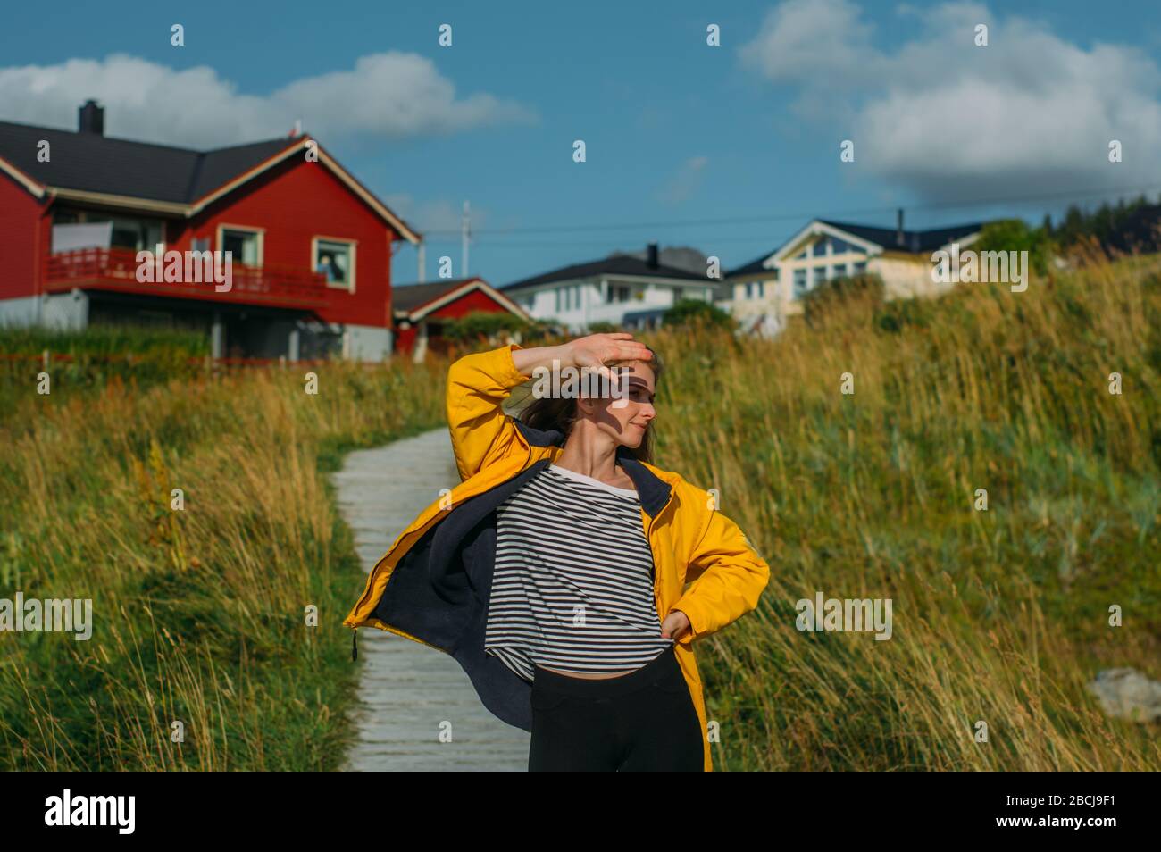 Ragazza in giacca gialla sul percorso per le case sulle isole Lofoten, Norvegia Foto Stock