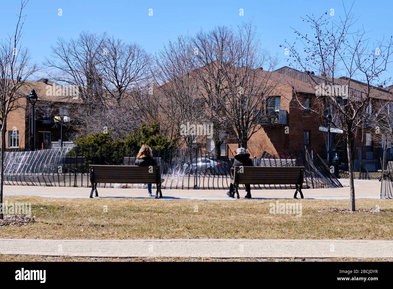 Due donne sedute su panchine separate nel parco per tenere il sociale distanziando a Montreal Foto Stock